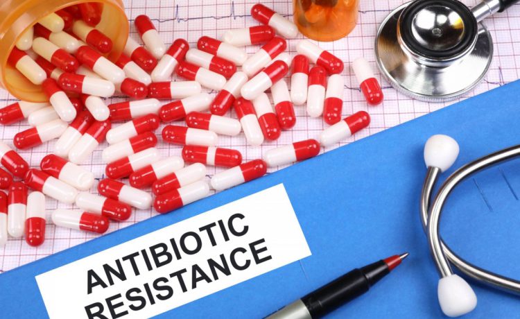 A folder labeled "Antibiotic Resistance" with a pen and stethoscope on it, adjacent to red and white pills spilling out of an orange pill bottle.