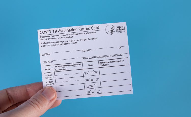 Hand holding a COVID-19 vaccination record card against a blue background